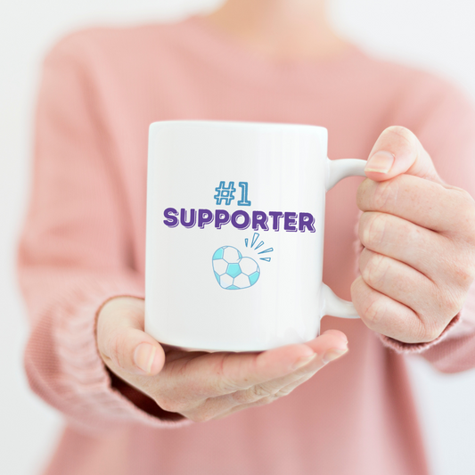 White mug with the text in blue #1 Supporter with a graphic of a heart with a vintage soccer ball print.