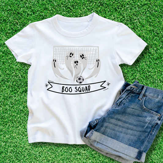 White t-shirt laying on the green grass with grey ghosts playing soccer with a goal behind and the text Boo Squad.