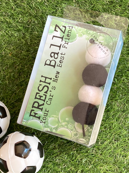 Black and white woolen balls in clear plastic case to hang in the car laying on grass with soccer ball props