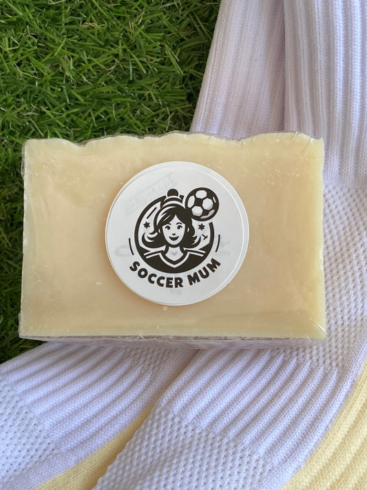 Block of cream soap with a soccer mum logo laying on  pair of clean socks. All on a background of grass.