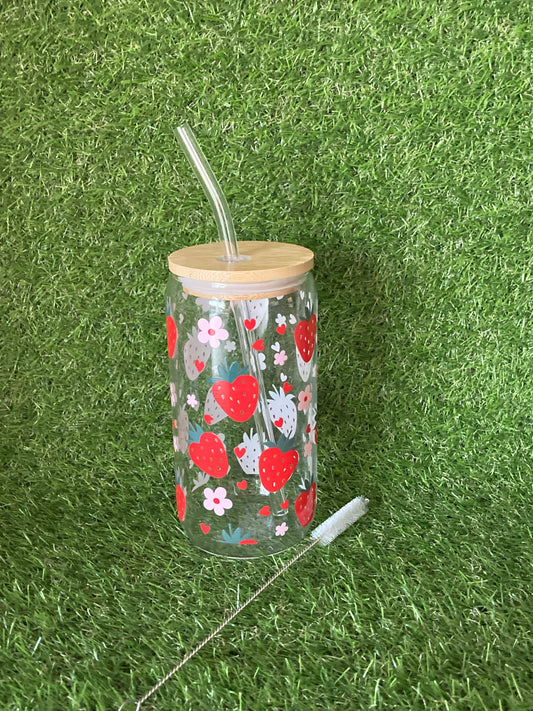 Clear glass can tumbler featuring strawberry and pink flower print with bamboo lid, clear straw and straw cleaner on green grass background.