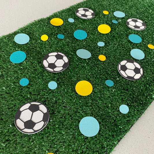 Yellow and blue round paper discs with black and white paper soccer balls scattered across synthetic grass